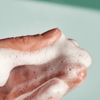 Mousse onctueuse sur une main, symbolisant la propreté et les soins délicats de la peau avec les produits nettoyants doux.